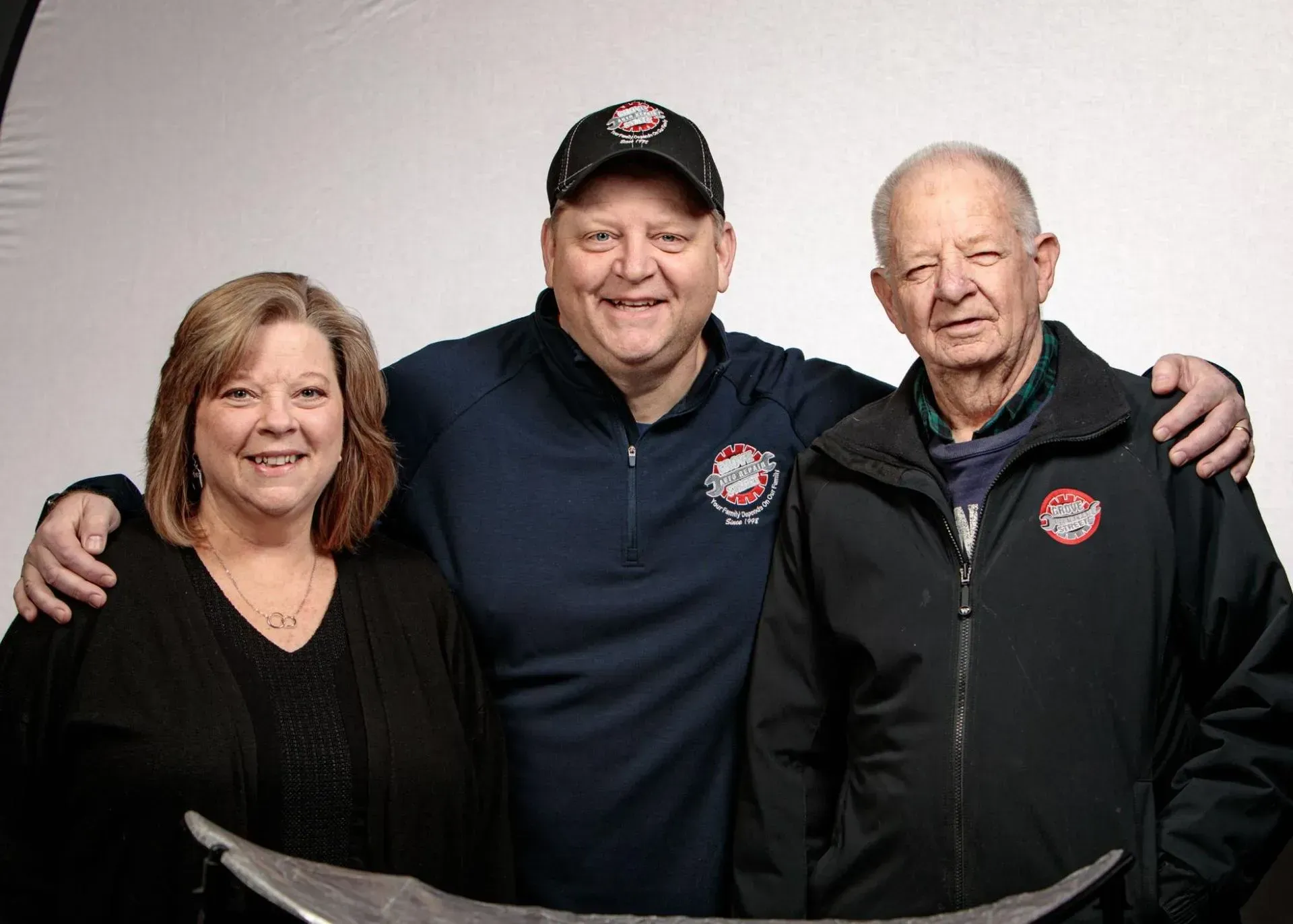 Three smiling people in dark jackets and caps posing together against a plain background
