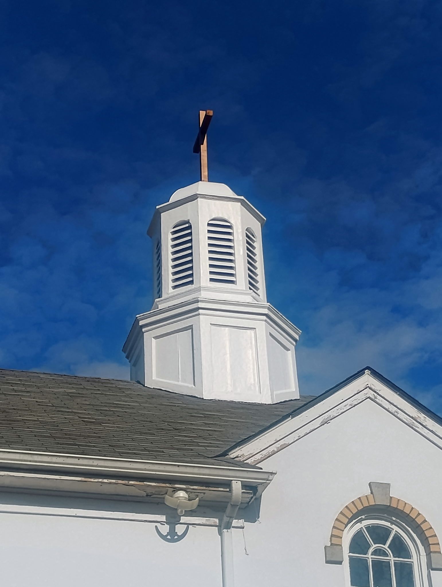 White church steeple with cross against a blue sky.