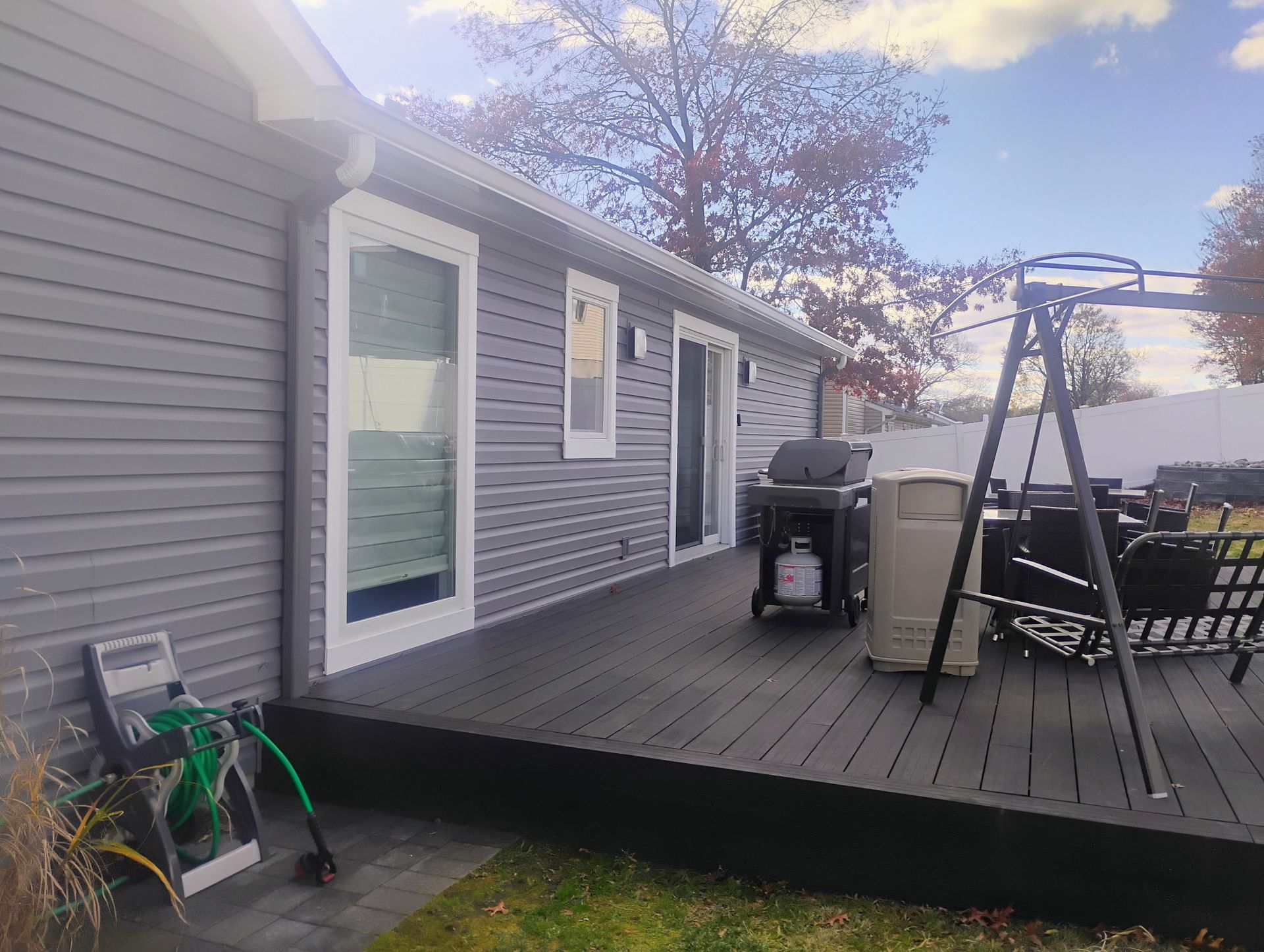 Gray house with dark deck, grill, swing set, and blue sky.