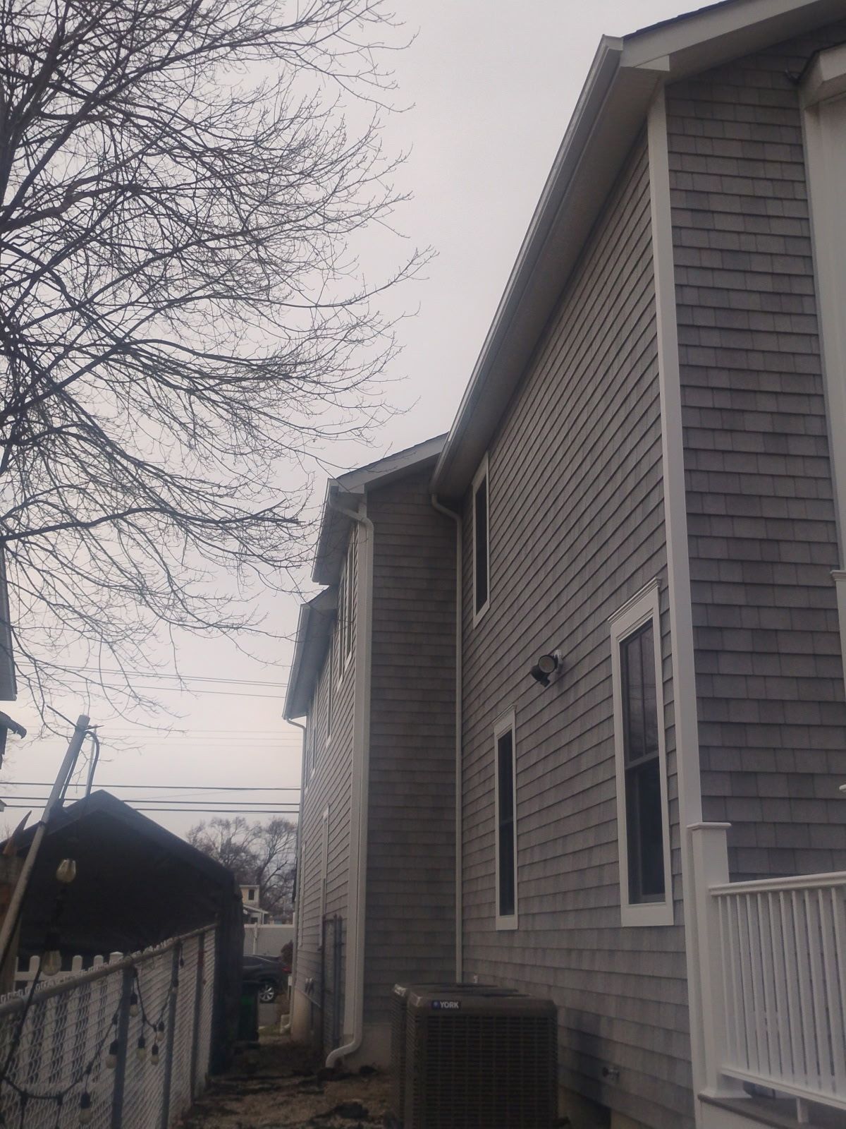 Gray shingled house exterior with a cloudy sky and bare tree.