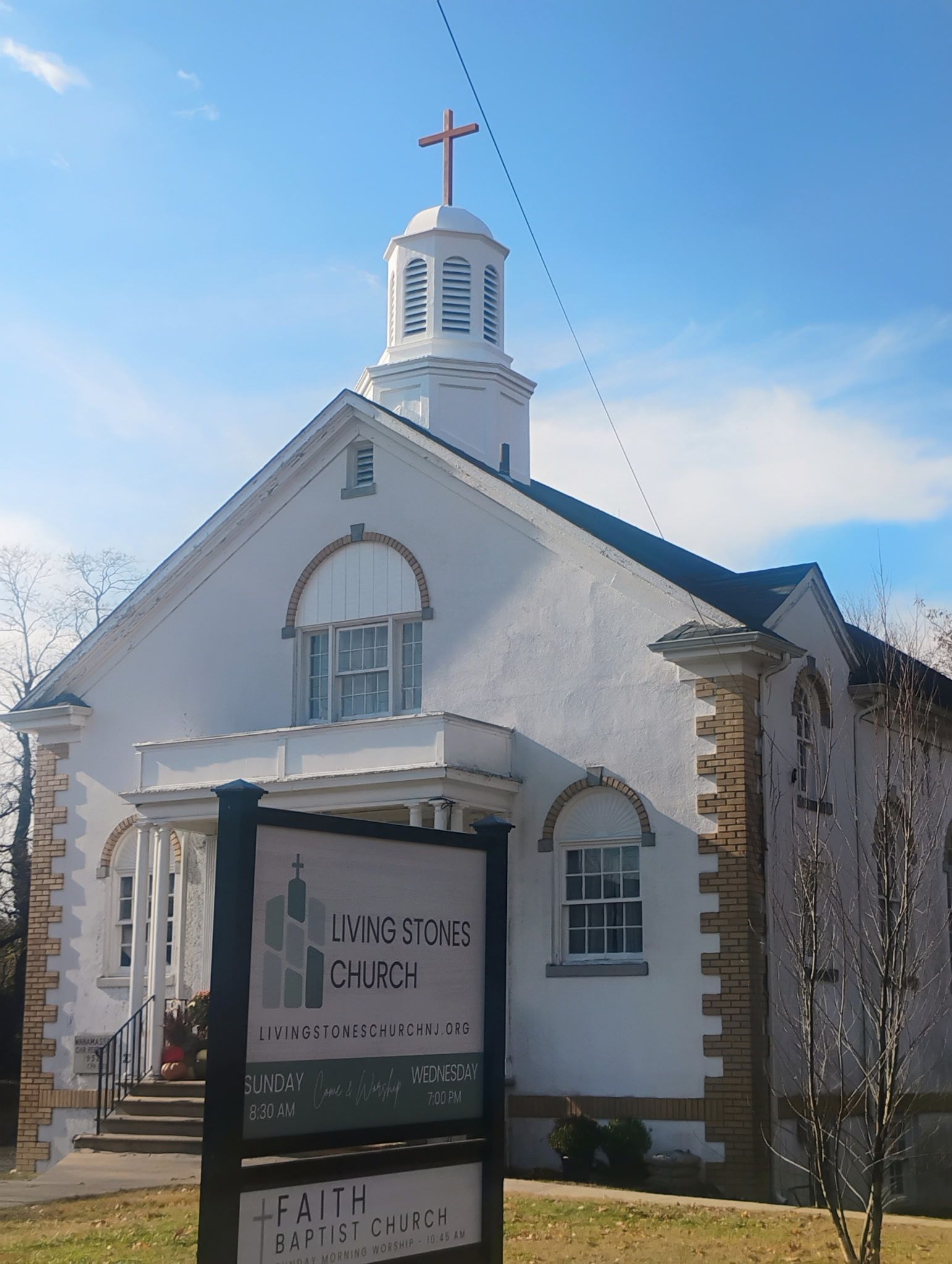 White church building with steeple and red cross, a sign in front.