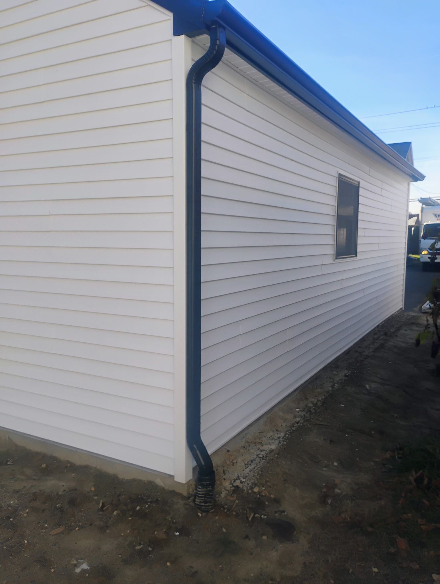 White clapboard siding on a building with black gutters and a dark roof; a small window is visible.