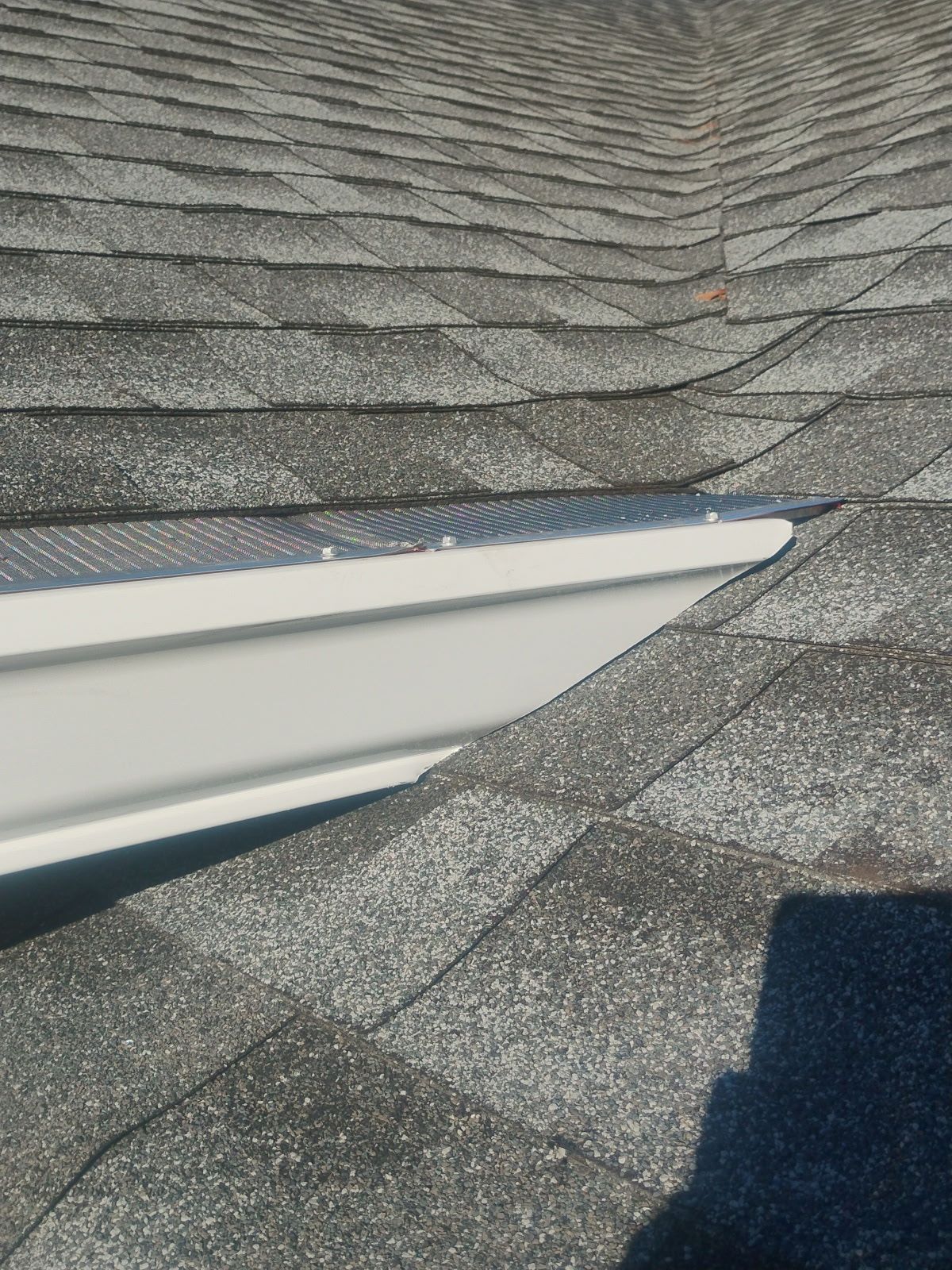 White gutter and guard installed on a dark gray shingle roof, angled view.