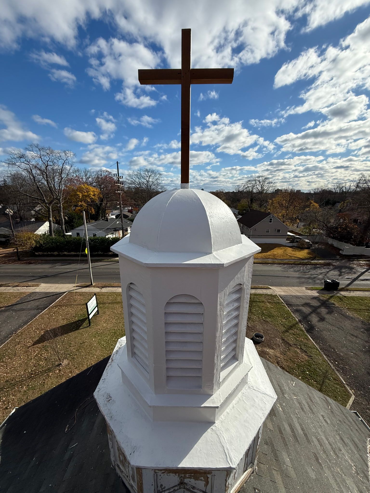 A church steeple with a cross on top against a cloudy blue sky.