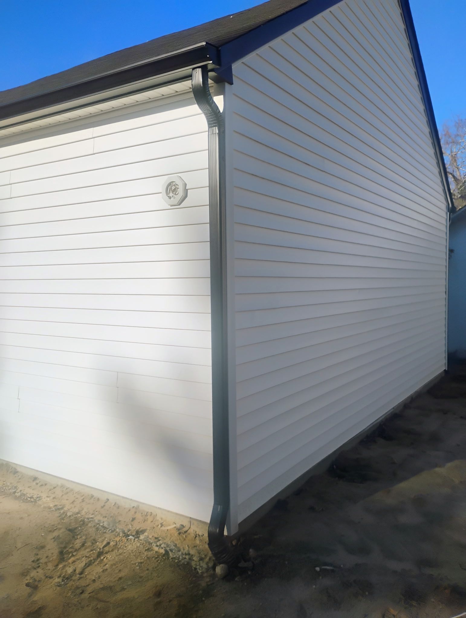 White building with black trim and a gutter, on a sunny day.