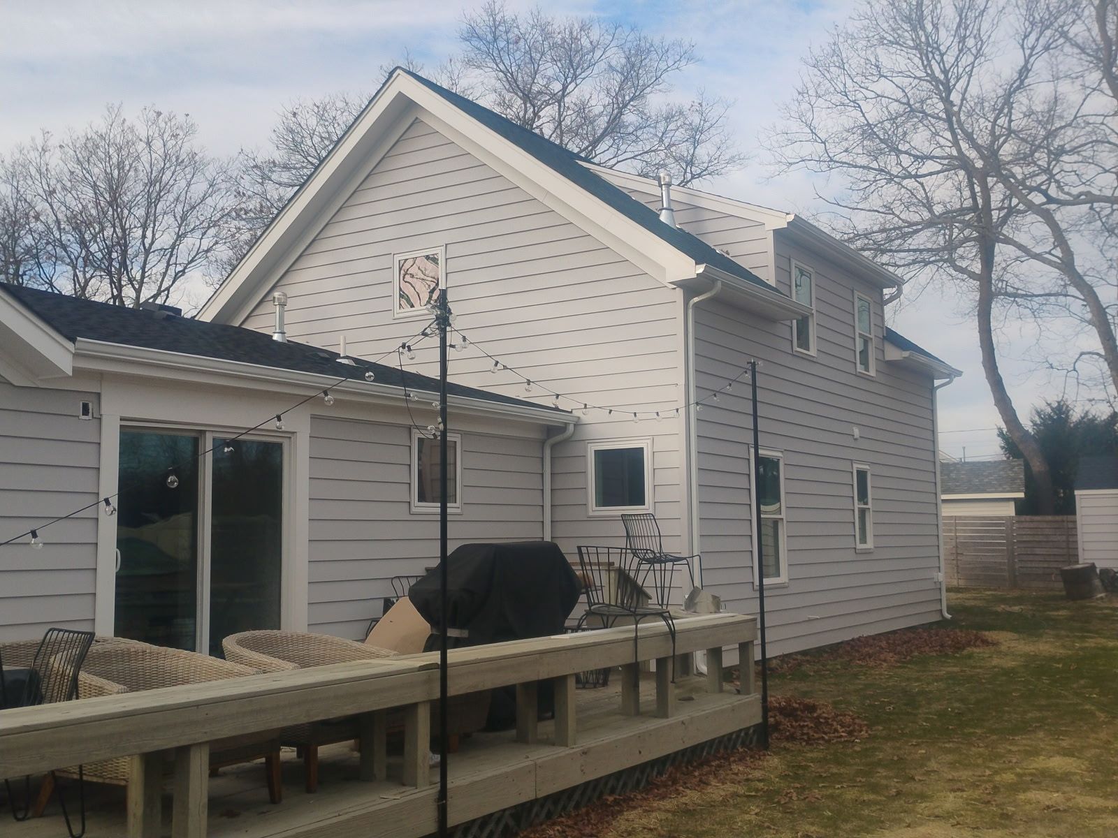Gray house with a deck in a backyard, trees in the background.