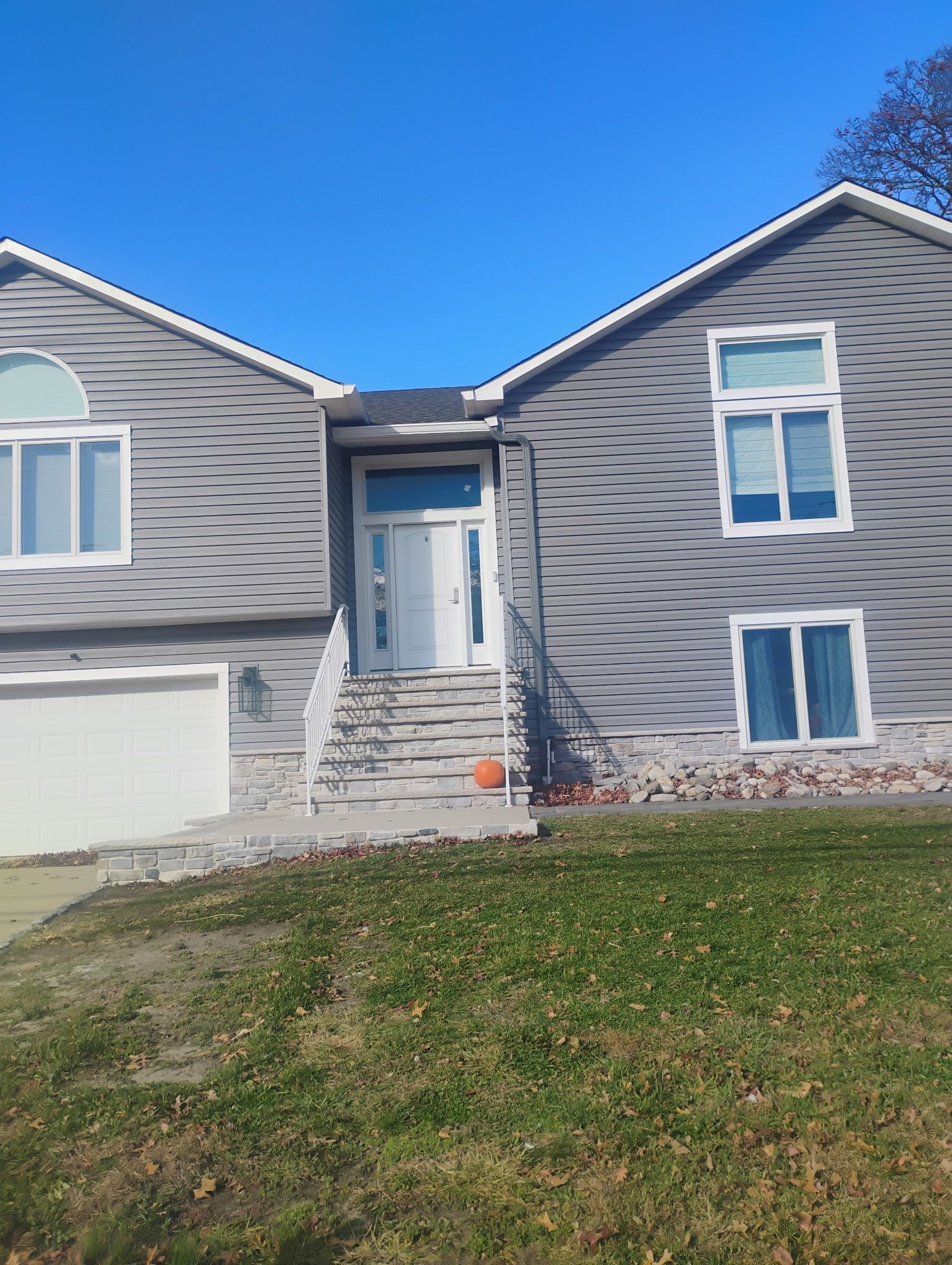 Gray house with white trim, arched and rectangular windows, white door, and orange pumpkin on the steps.