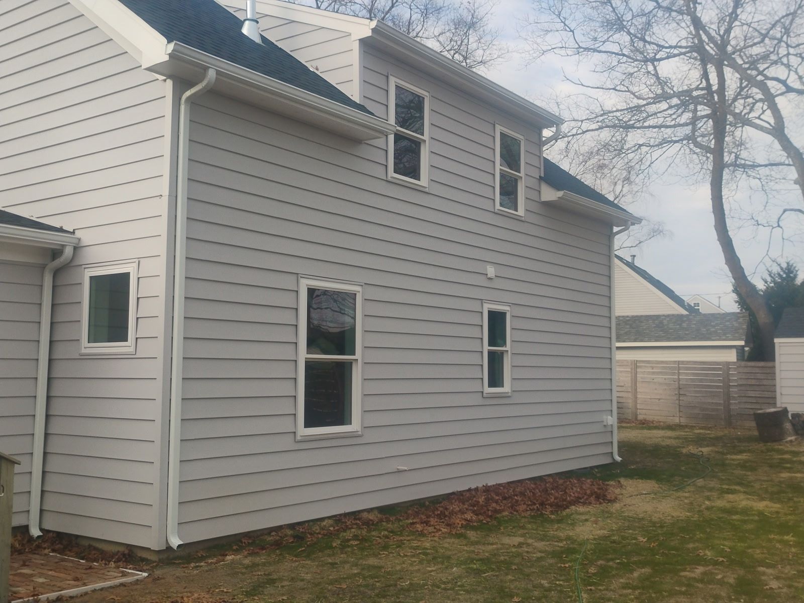 Side view of a two-story house with gray siding, white trim, and multiple windows.