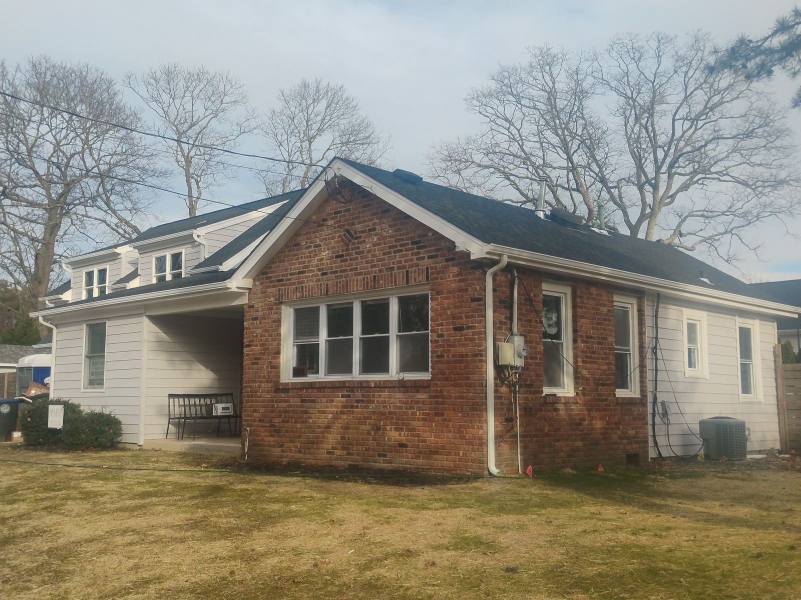 House with brick and white siding, windows, and dark roof under a cloudy sky.