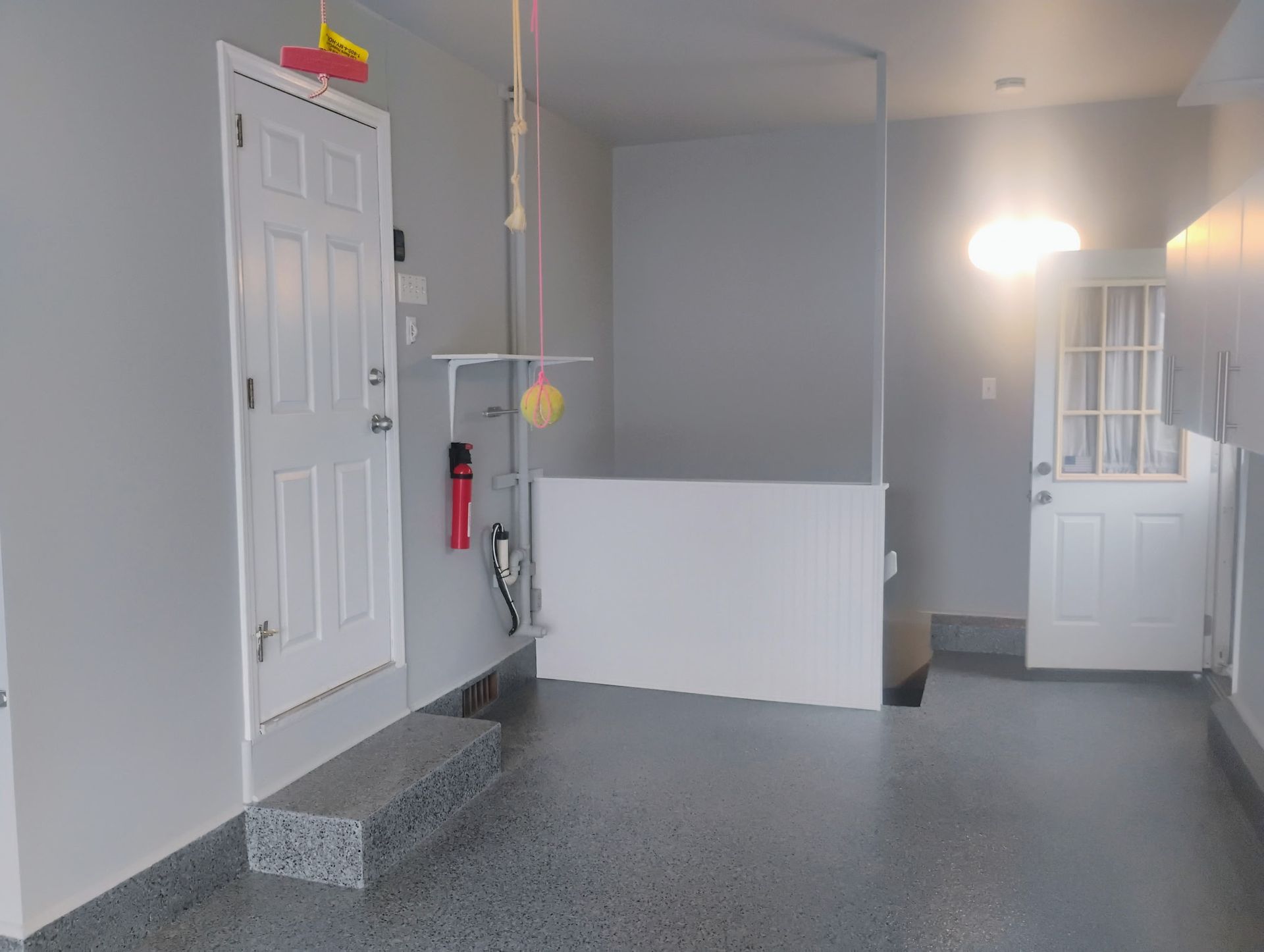 A light-gray painted garage with two white doors, a granite step, and a white dog bath.