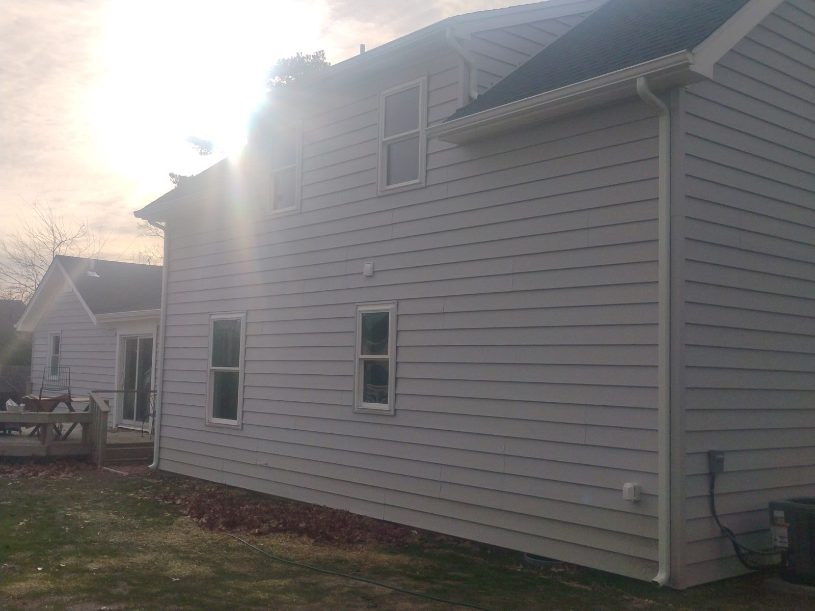 Side view of a light gray house with white trim, set against a cloudy sky.