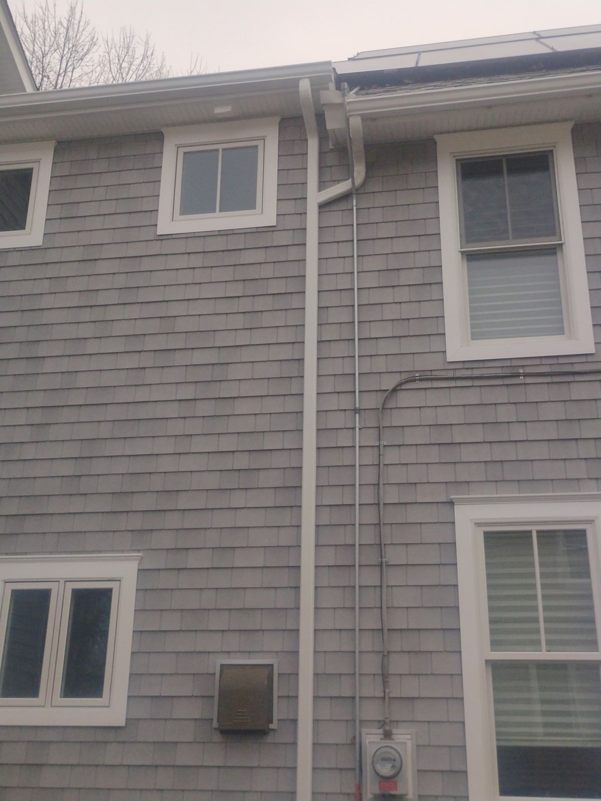 Gray shingled house exterior with white trim windows and a gutter downspout.
