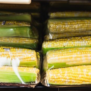 A bunch of corn on the cob wrapped in plastic on a shelf.