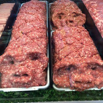 Two trays of ground beef with faces on them in a butcher shop.