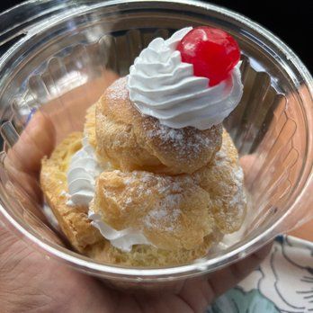 A person is holding a small dessert with whipped cream and a cherry on top.