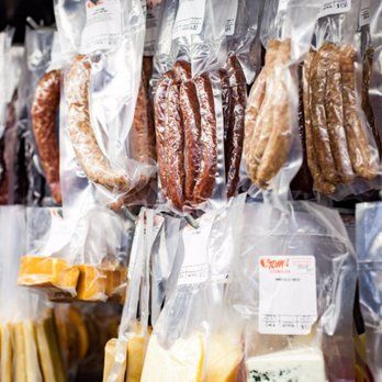 A variety of sausages and cheeses in plastic bags hanging on a wall.