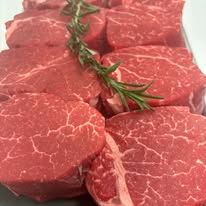 A close up of a pile of raw steaks with rosemary.