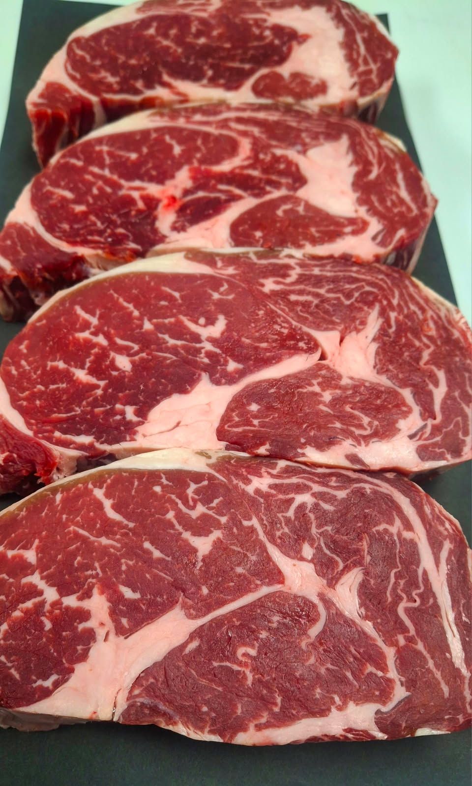 Four steaks are lined up on a black cutting board.