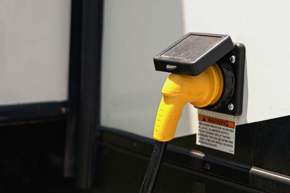Yellow RV Power Cord Plugged Into a Black Inlet on a White Surface — DC Active Electrical in Brighton, QLD