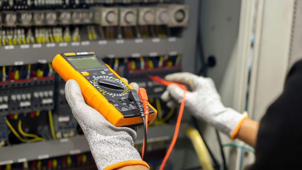 Person Wearing Gloves Using a Multimeter to Test Electrical Wiring in a Control Panel — DC Active Electrical in Geebung, QLD