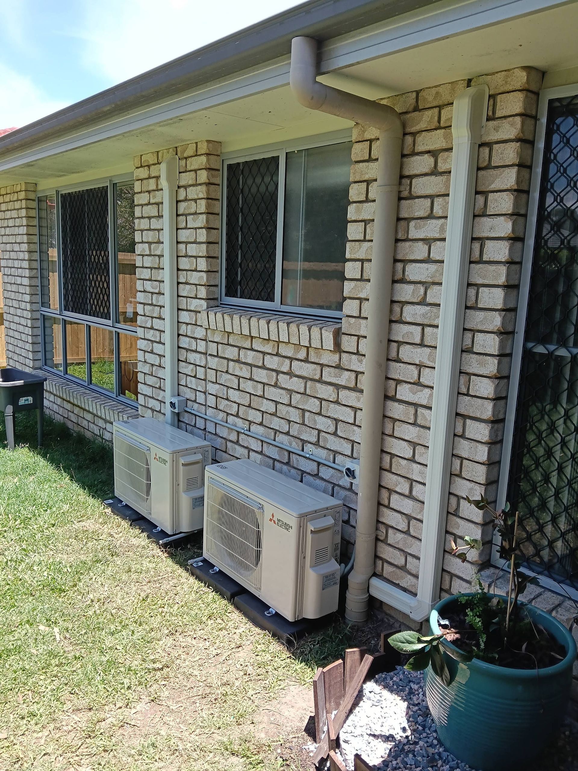 Two Air Conditioning Units Mounted on a Brick Wall, With a Gutter and Windows Visible — DC Active Electrical in Geebung, QLD