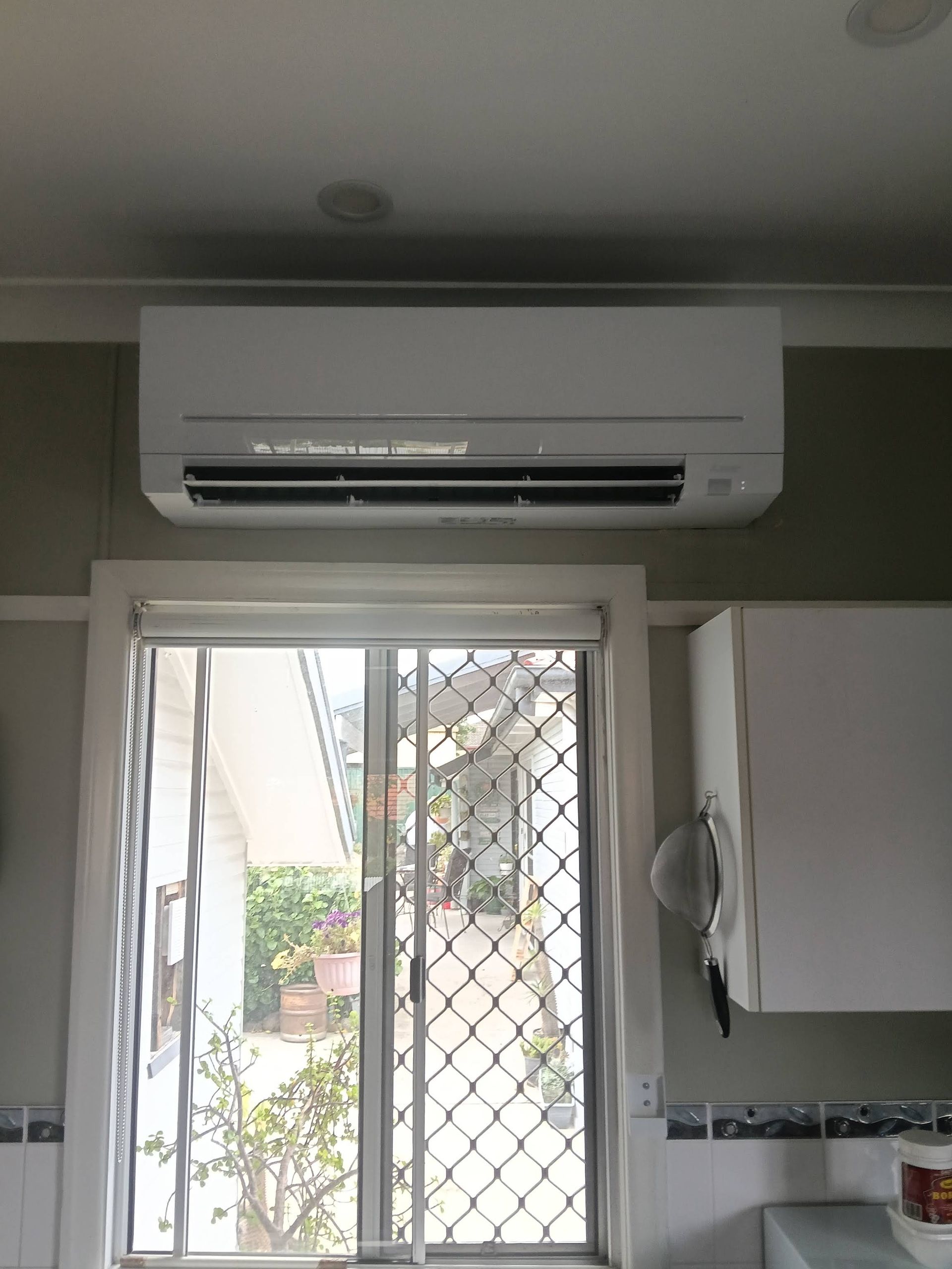 White Air Conditioner Mounted Above a Window in a Kitchen — DC Active Electrical in Albany Creek, QLD