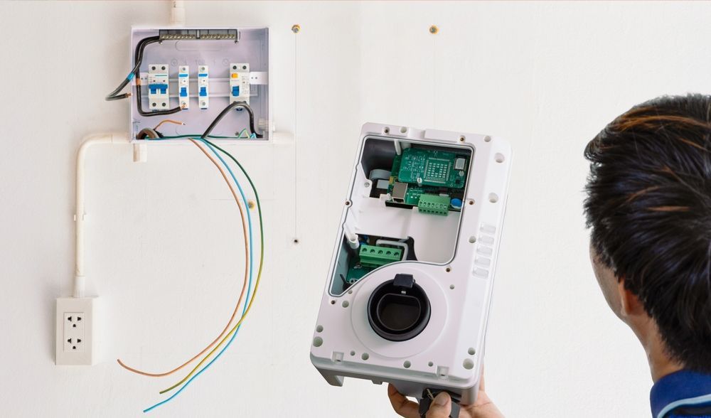 Person Installing an Electric Vehicle Charger on a White Wall — DC Active Electrical in Geebung, QLD