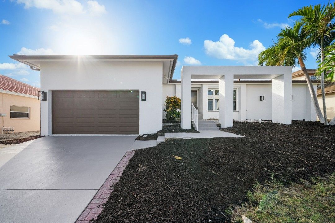 A large white house is surrounded by palm trees and flowers.