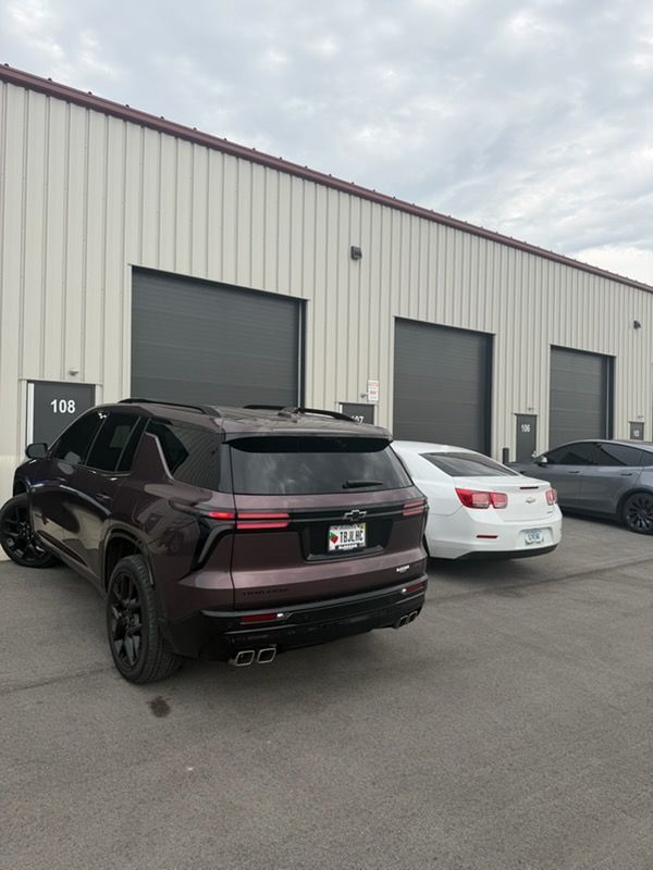 Parking lot with a maroon SUV, white sedan, and gray car outside an industrial warehouse.