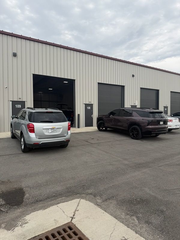 Industrial building exterior with parked silver SUV and black pickup in front of open garage bays