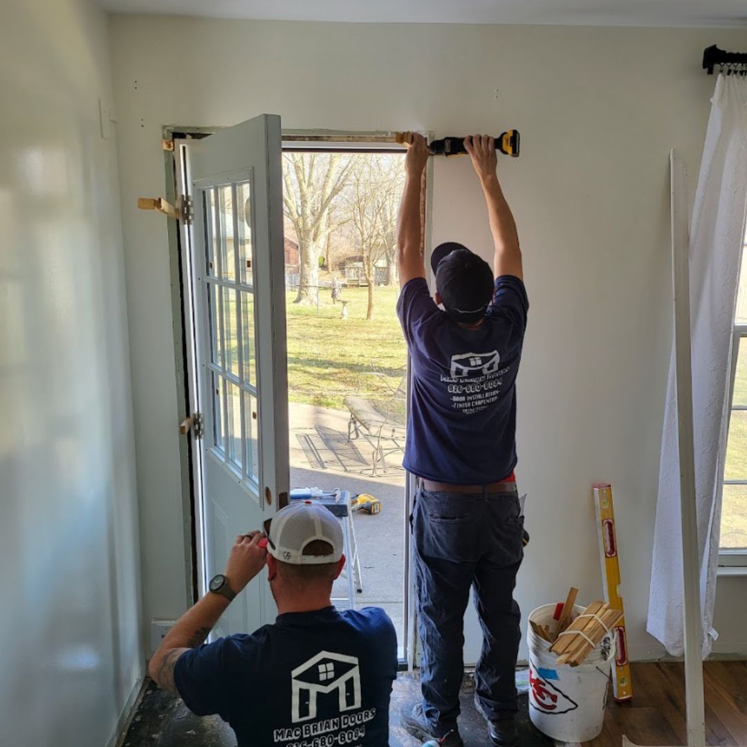 Two men are working on a door in a room.
