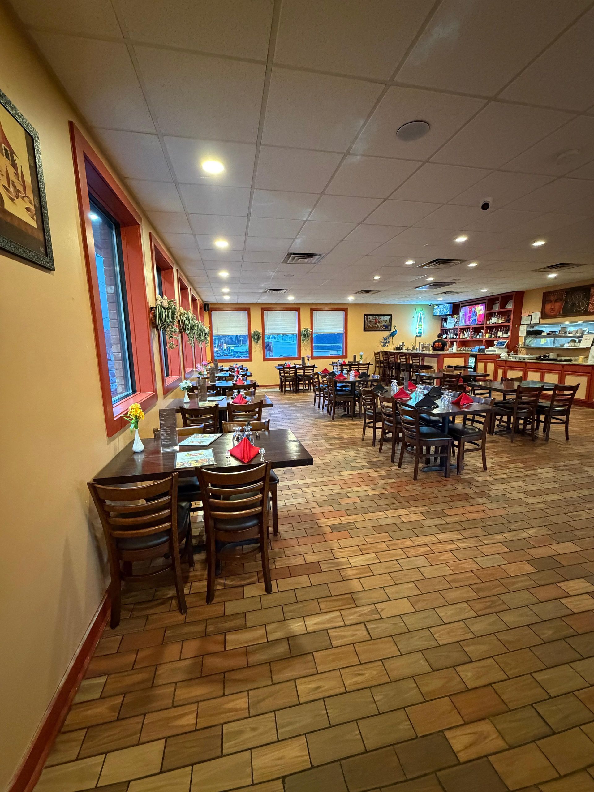 Interior of a restaurant with brick floors, wooden tables and chairs, and a bar in the background labeled
