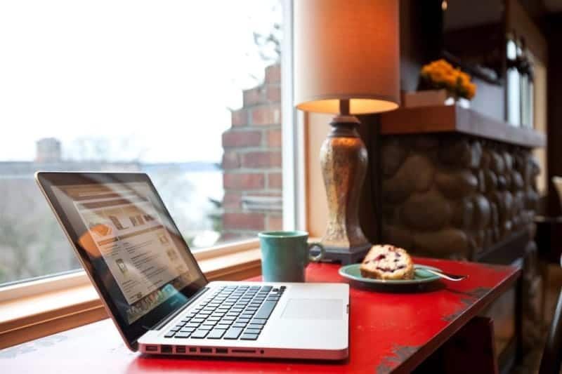 A laptop is sitting on a red table next to a plate of food and a lamp.