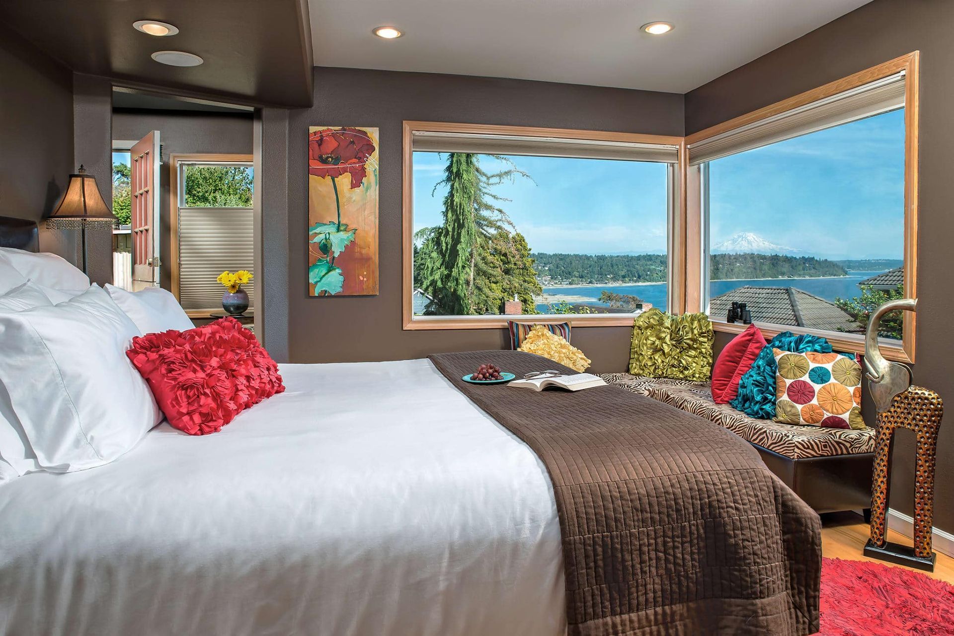 A bedroom with a large bed and a large window with a view of the ocean.