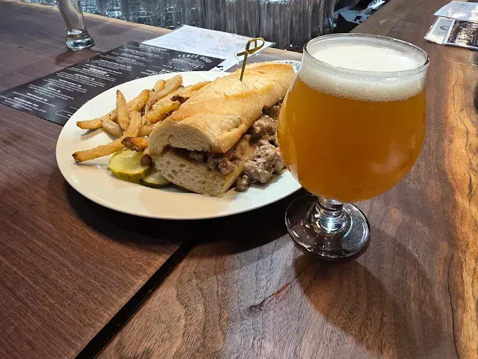 Beer and sandwich on a wooden table, with fries on a white plate in a pub.