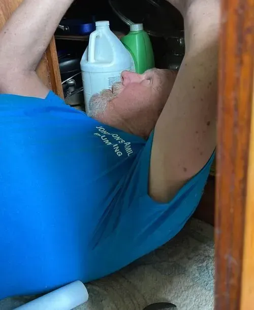 Man in blue shirt reaching into cabinet. White jug and green bottle visible.