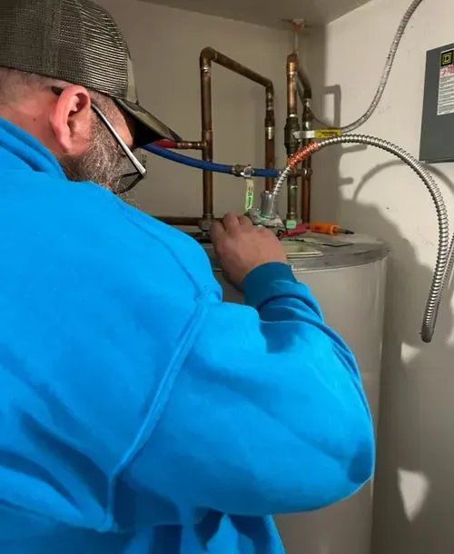 Plumber in a blue shirt working on a water heater, copper pipes visible.