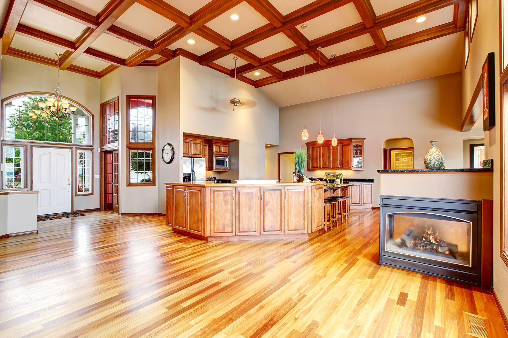 Spacious, well-lit living room with hardwood floors, a coffered ceiling, a kitchen island, and a fireplace.