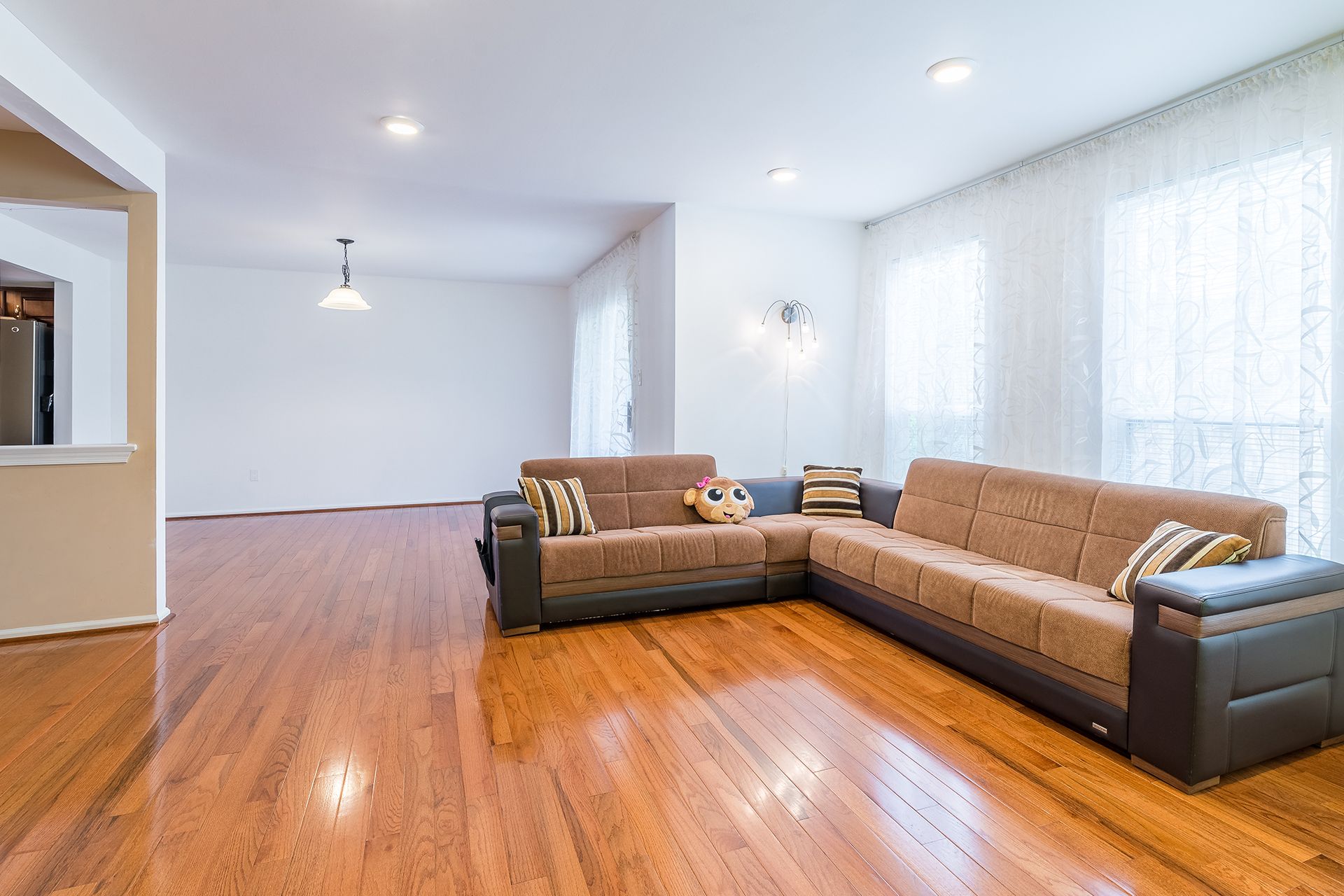 L-shaped sofa in a living room with hardwood floors and sheer curtains.