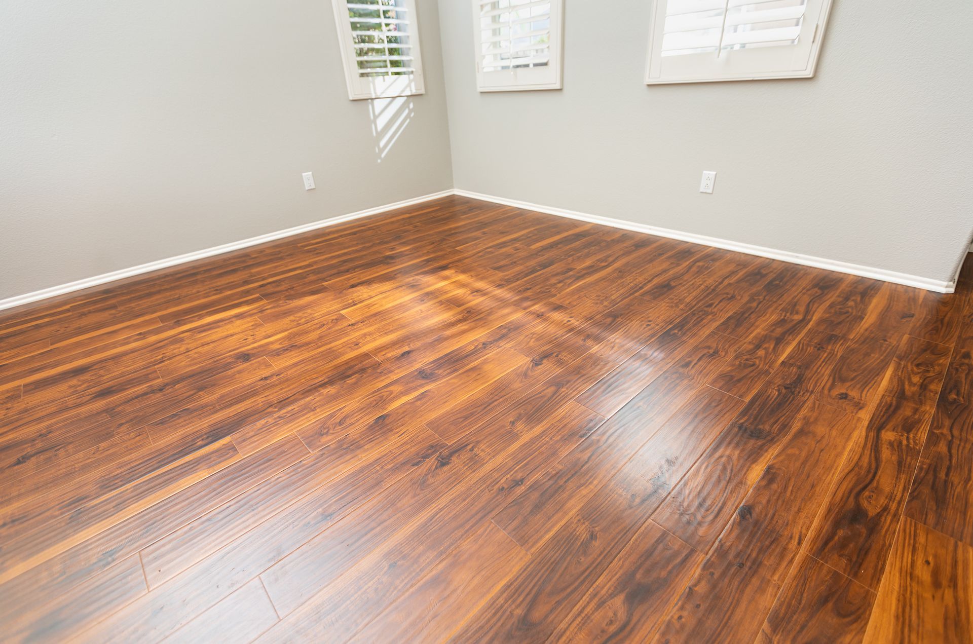 Empty room with dark wood flooring, gray walls, and three windows with closed shutters.