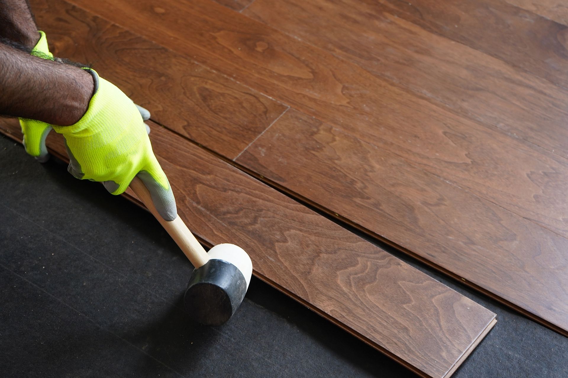Person installing dark wood flooring, using a hammer and gloves.