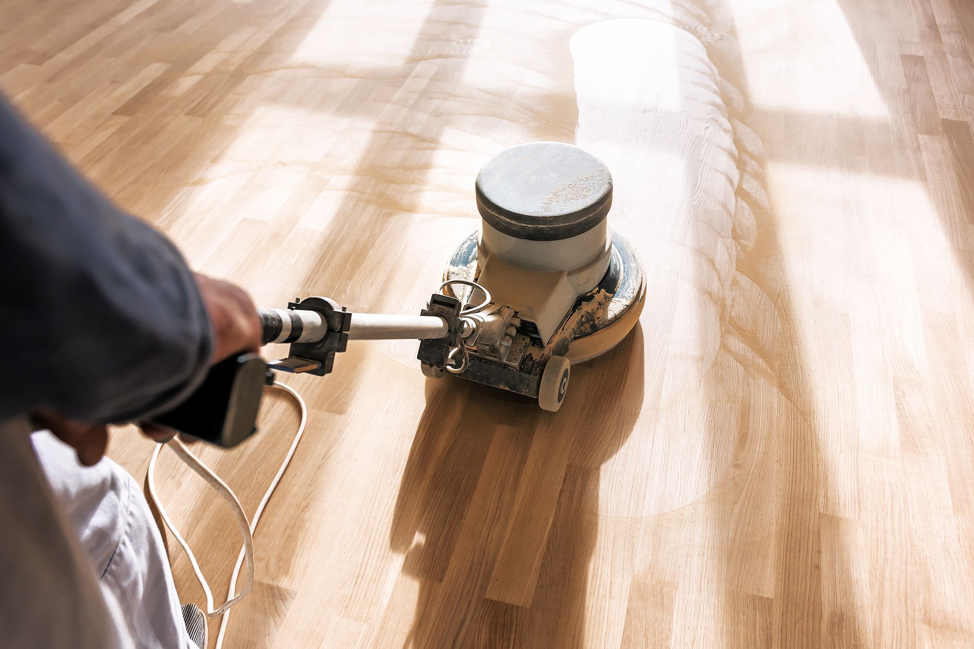 Person using a floor sander on a light-colored wooden floor, sanding for refinishing.