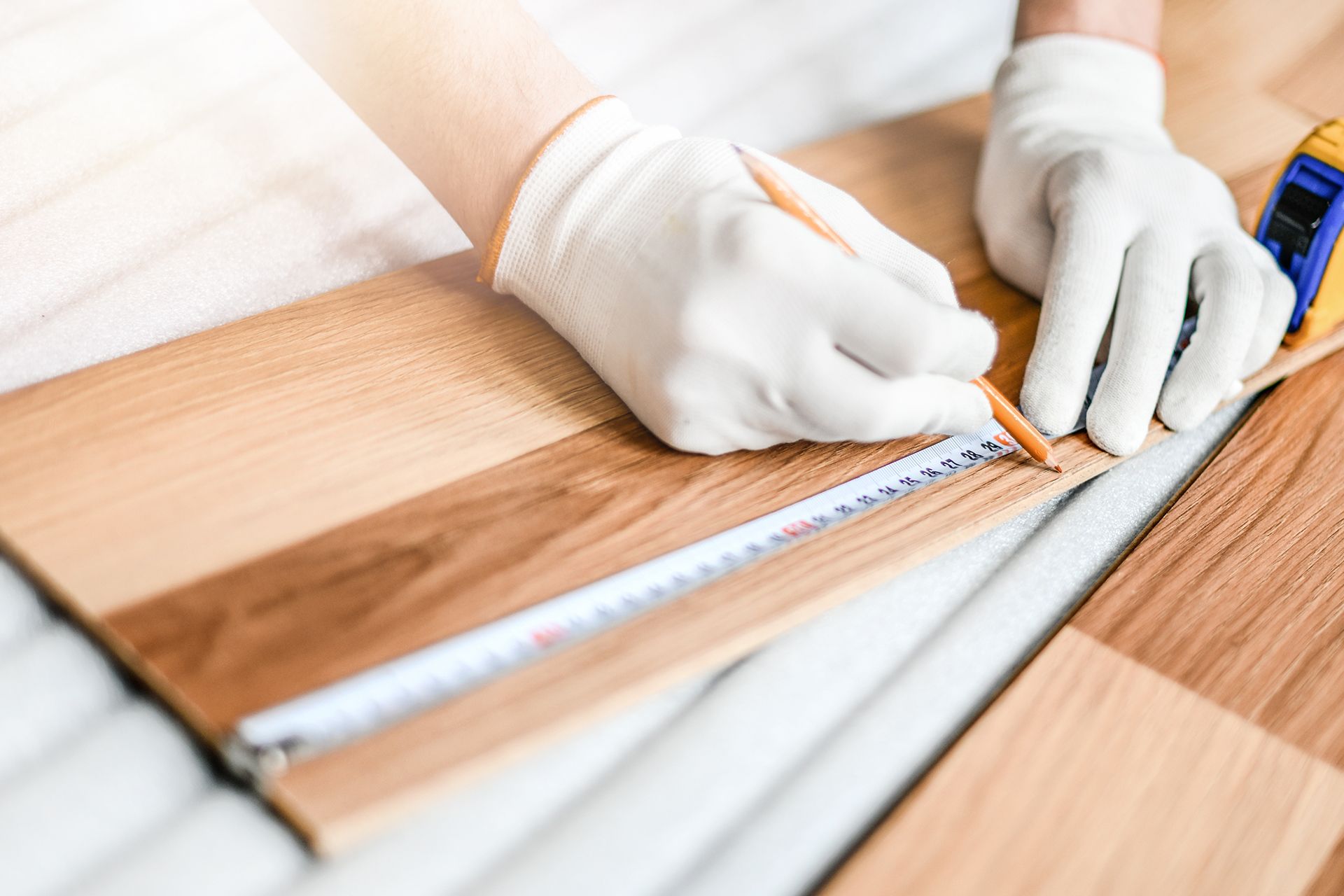 Person wearing gloves marks wood flooring with pencil and measuring tape.