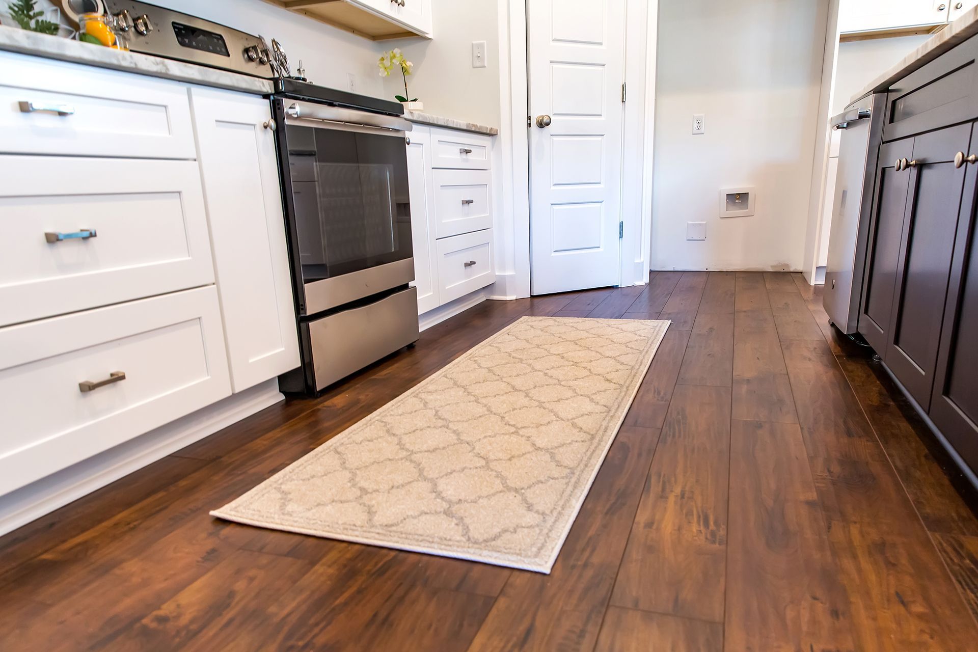 Kitchen with white cabinets, stainless steel oven, wood floors, and a patterned rug.