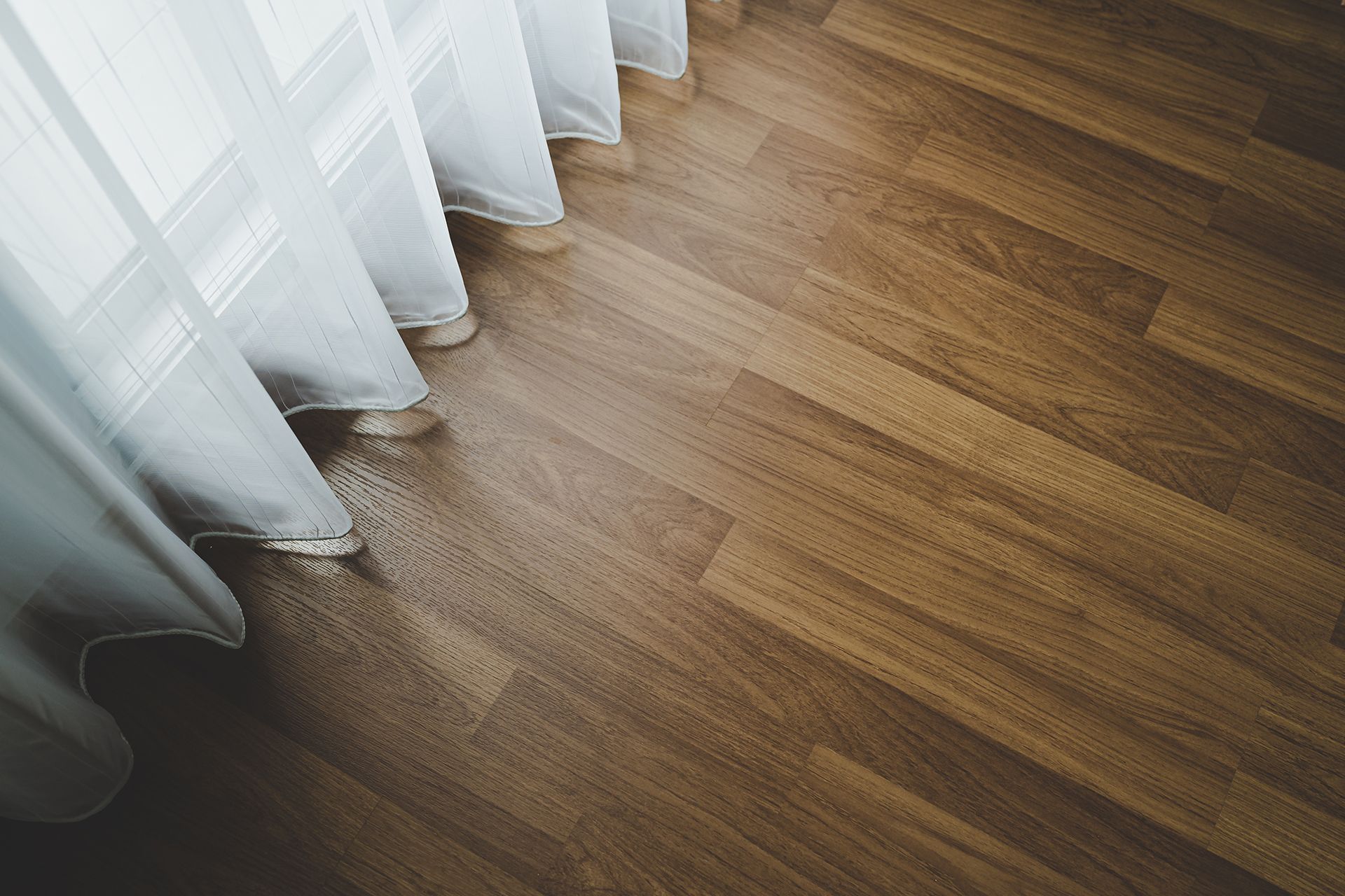 White sheer curtain draped over light brown hardwood floor.