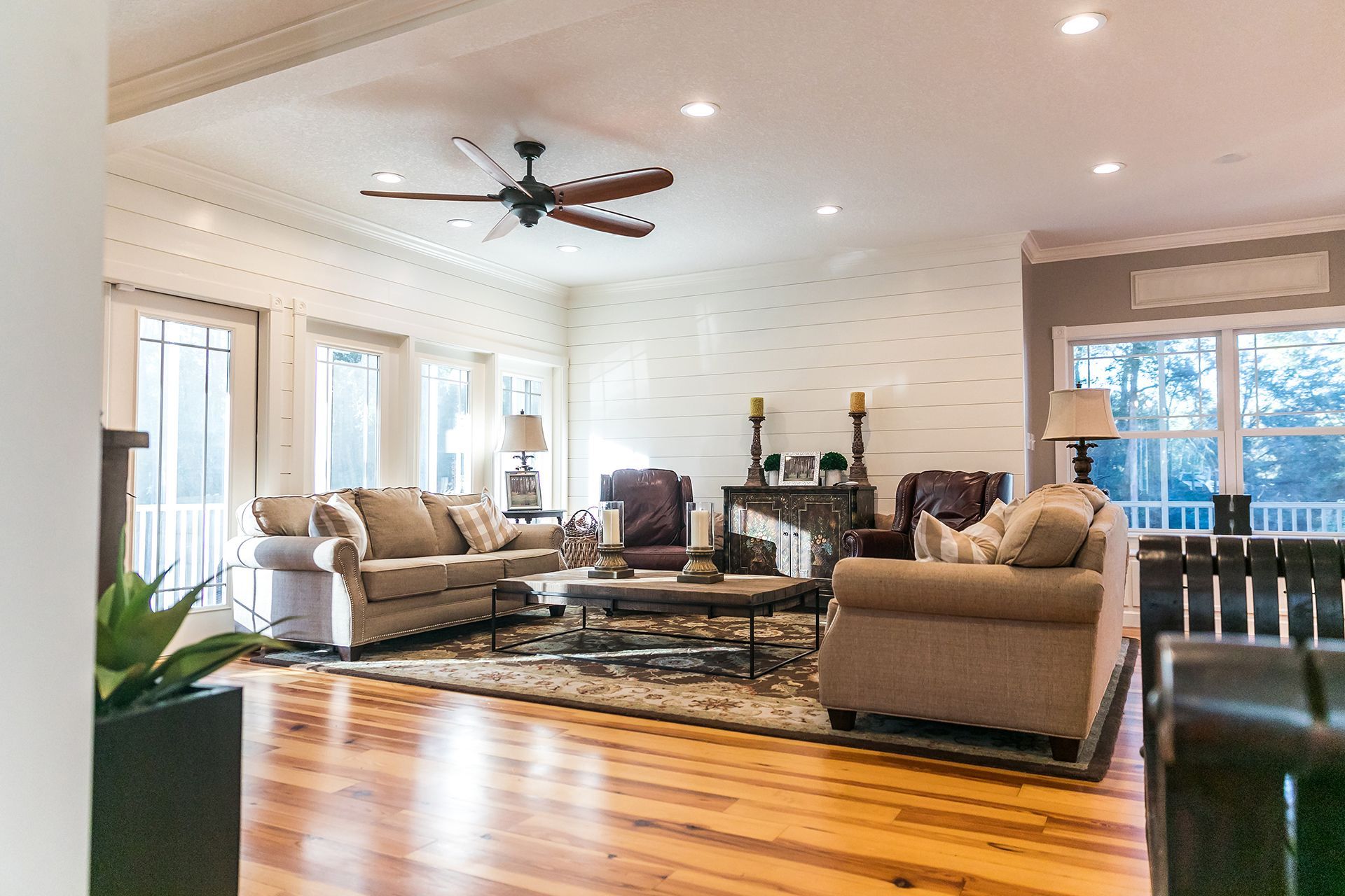 Spacious living room with light-colored furniture, hardwood floors, and large windows.
