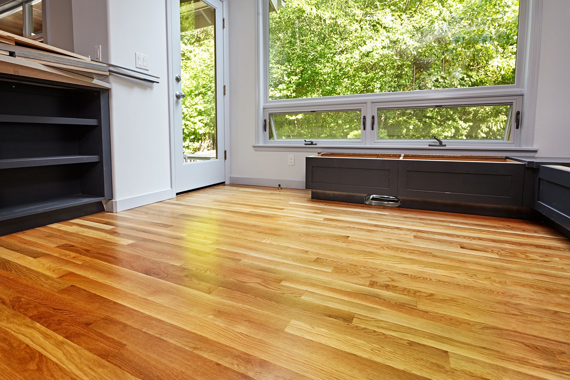 Hardwood floor in a room with a window overlooking trees; a dark cabinet is in the background.