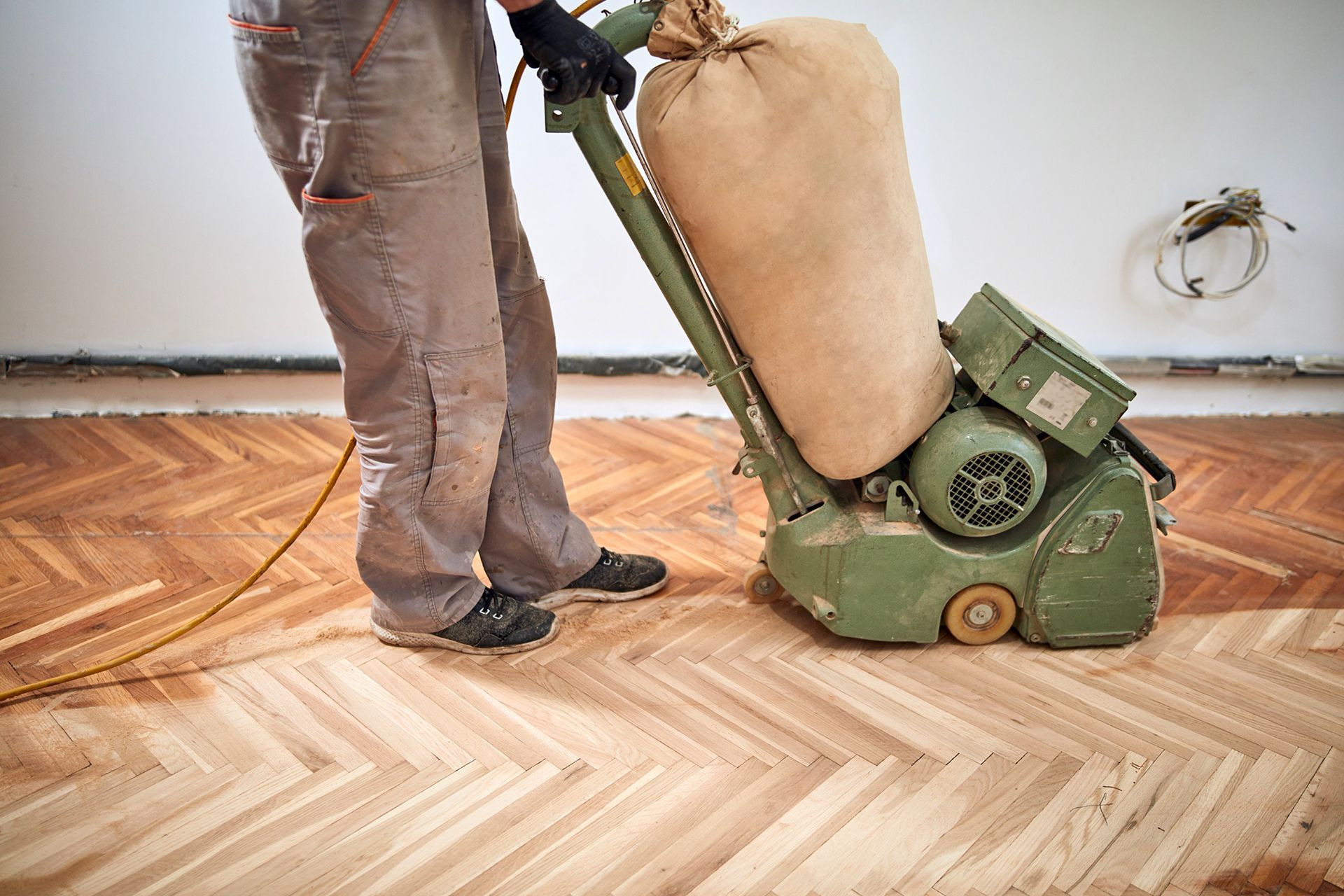 Person sanding a wooden herringbone floor with a large industrial sander, indoors.