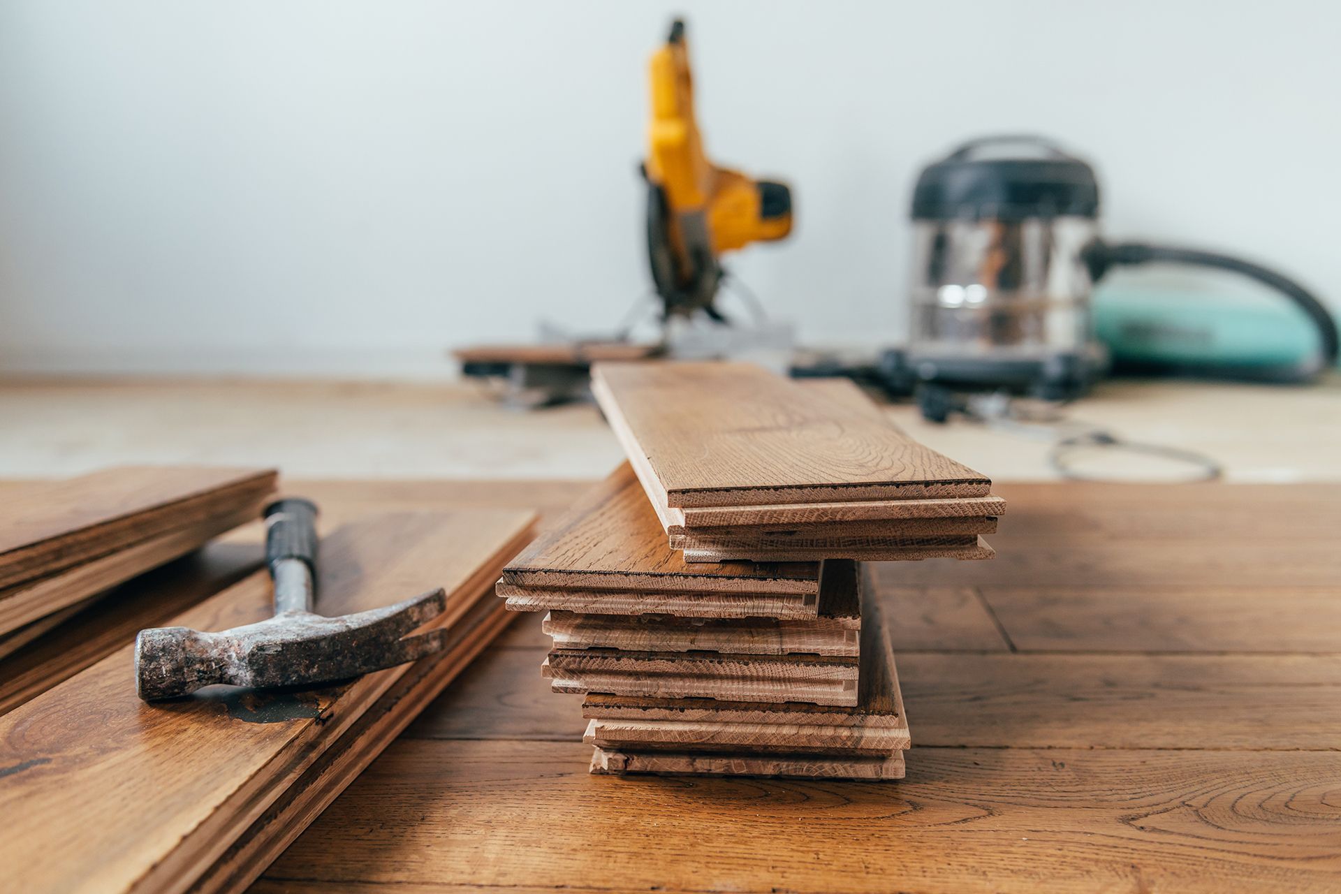 Wooden floorboards stacked with tools: hammer, saw, and vacuum, likely for installation.