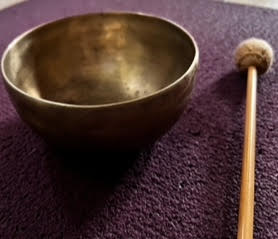A bowl and a wooden stick are sitting on a purple carpet.